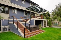 a house with a deck and hot tub on the lawn next to stairs that lead up to it