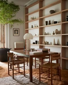 a dining room table and chairs in front of a book shelf with vases on it