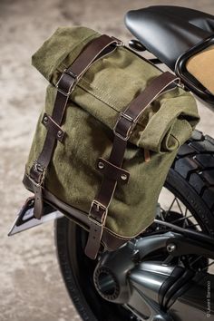 a green bag sitting on the back of a motorbike with leather straps and buckles