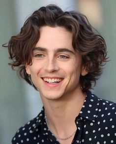 a young man with curly hair smiles at the camera while wearing a polka dot shirt