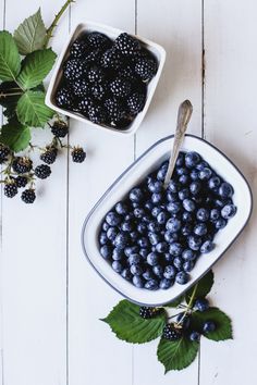 blueberries and blackberries in a bowl on a white wooden table with green leaves