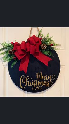 a merry christmas sign hanging on a door with red bows and pineconifers