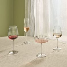 three wine glasses sitting on top of a table next to each other in front of a window