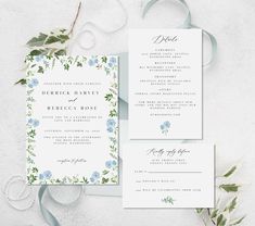 wedding stationery with blue flowers and greenery on white paper next to green ribbon