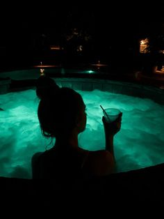 a woman sitting in the middle of a pool holding a drink