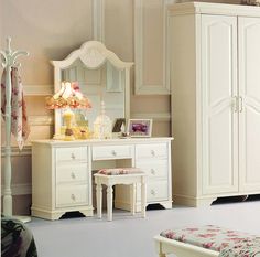 a white dresser with a mirror and lamp on top of it next to a bed