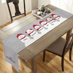 a christmas table runner with snowmen and santa hats on it, sitting at a dining room table