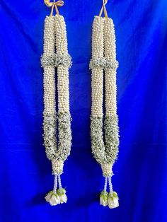 two corn cobs with flowers hanging from hooks on a blue background in front of a blue backdrop