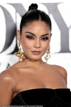 a woman in a black dress with large gold earrings on her head and dark eyeshadow