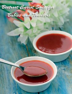 two white bowls filled with red sauce on top of a blue wooden table next to flowers