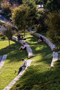 several people sitting on the grass in a park with stone walls and steps leading up to them