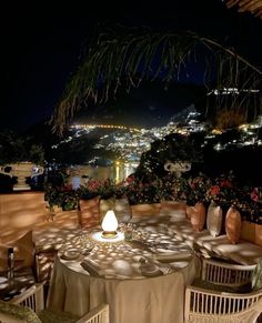 an outdoor dining area with tables and chairs overlooking the city lights at night in the distance