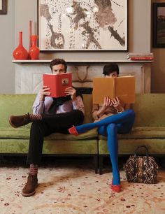 two people sitting on a couch with books in their hands and one person holding a book