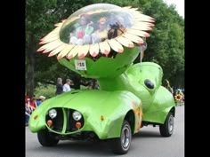 a green car with people riding in it's back and on the front wheel