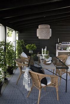 an outdoor dining area with wicker furniture and plants on the table, in front of a black wall