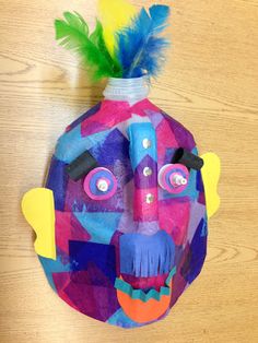 a colorful mask hanging on the wall with feathers in it's mouth and eyes