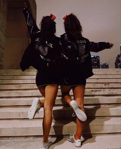 two girls in black jackets and white shoes are walking up some steps with their arms outstretched