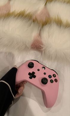 a pink controller being held by someone's hand on top of a white bed