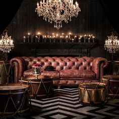 a living room with leather furniture and chandelier hanging from the ceiling in front of a fireplace