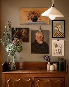 an old man's portrait hangs on the wall above a dresser with vases and flowers