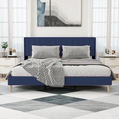 a bed with blue headboard and pillows in a white room next to two windows