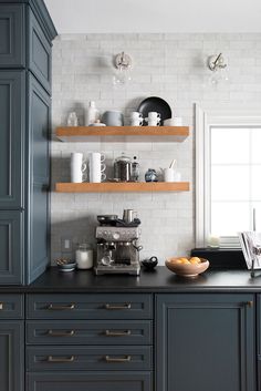 a kitchen with blue cabinets and black counter tops, white brick walls and open shelving