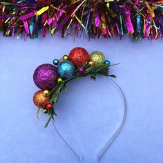 a headband with christmas ornaments and tinsel on the top, next to a purple background