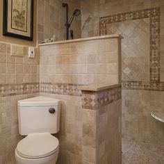 a white toilet sitting inside of a bathroom next to a walk in shower and tiled walls