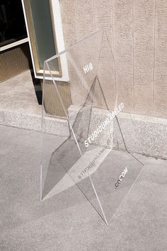 a clear acrylic sculpture sitting on the ground in front of a building with words written underneath it