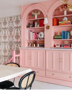 a dining room with pink furniture and floral wallpaper on the walls, along with bookshelves