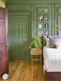 a bedroom with green painted walls and wooden flooring, along with a white bed