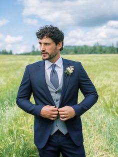 a man in a suit standing in the middle of a field with his hands on his chest