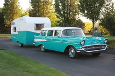 an old blue car parked next to a white and black trailer on the side of a road