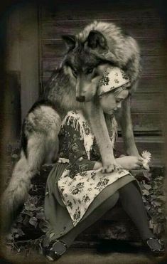 a woman sitting on the ground next to a wolf with her head in her hands