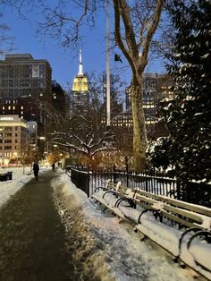 snow covered park benches in the middle of a city street at night with people walking on it