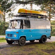 an old van with a surfboard on top parked in front of some trees and grass