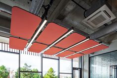 an empty room with lots of windows and bright red shades on the ceiling, along with large glass panes to let in natural light