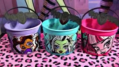 three buckets with cartoon characters painted on them sitting on a pink tablecloth and leopard print