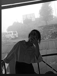 black and white photograph of a woman taking a selfie with her cell phone in front of a window