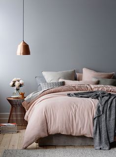 a bed with pink sheets and pillows next to a vase full of flowers on a table