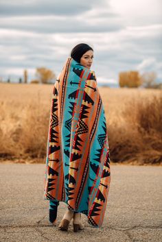 a woman standing in the middle of a road wearing a colorful blanket over her head