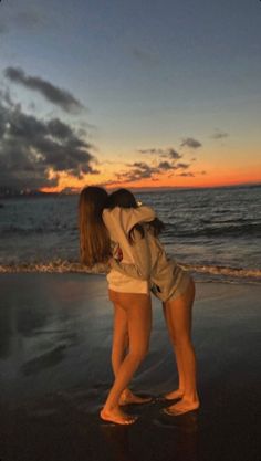 two girls are hugging on the beach at sunset