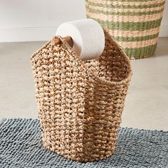 a basket with a roll of toilet paper in it sitting on a rug next to two baskets