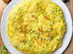 an omelet on a white plate with bread and parsley in the background