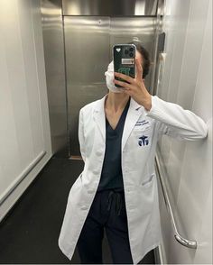 a woman taking a selfie in front of a mirror wearing a white lab coat