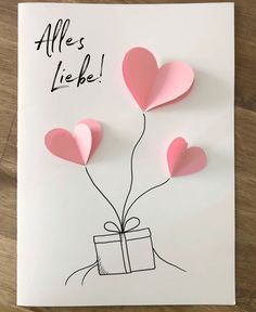 a card with pink paper hearts attached to it and a gift box in the middle