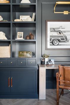 an office with blue bookcases, leather chair and wooden desk in front of it