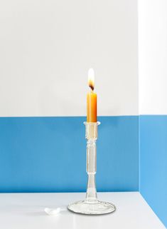 a single candle is lit in a clear glass vase on a white table against a blue and white wall