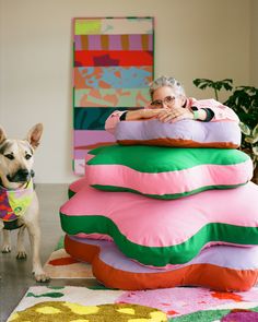 a dog standing next to a large pile of pillows on the floor in front of a woman