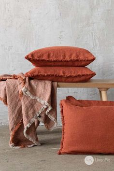 three orange pillows stacked on top of each other next to a wooden bench and stool